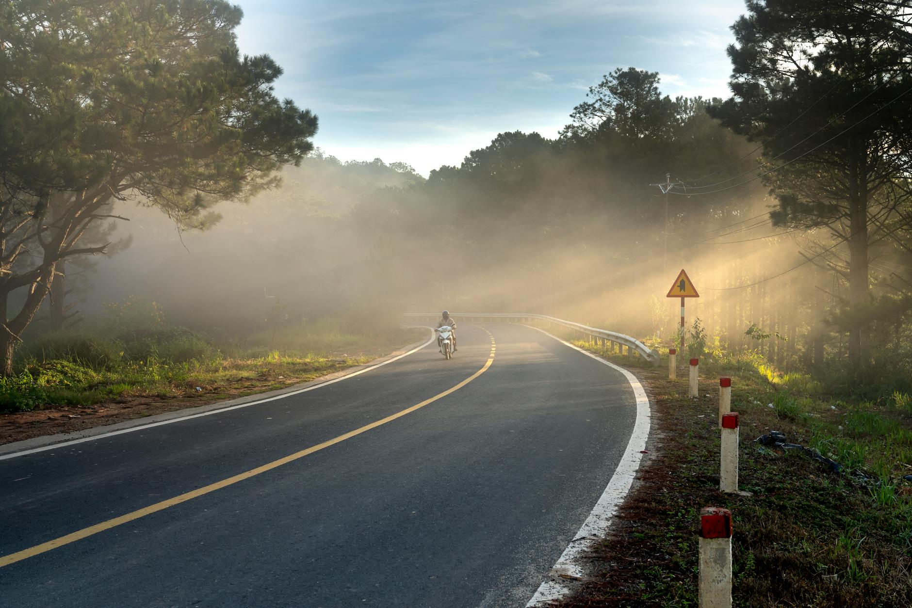 Motorcycle rider on a foggy highway road surrounded by forest
