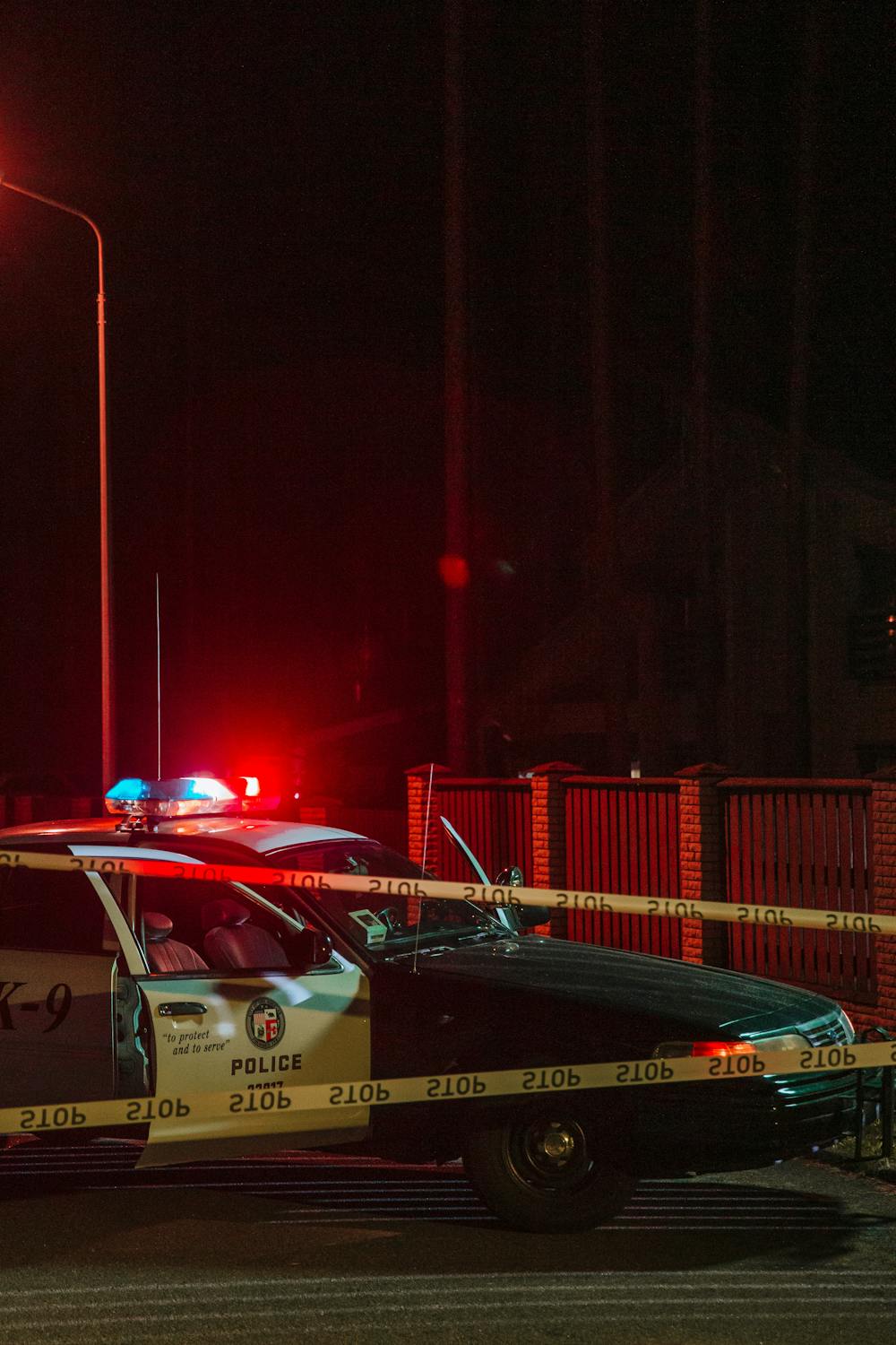 Police car with flashing lights at nighttime accident scene with caution tape